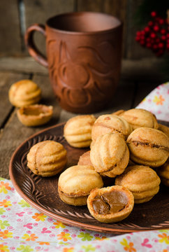 Walnuts shape cookies with condensed milk - dulce de leche in clay bowl on wooden rustic background. Selective focus