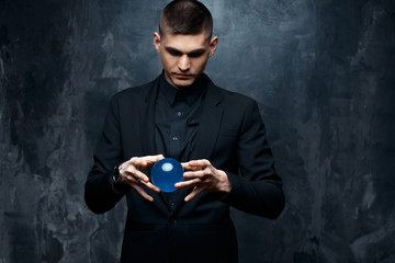 Magician young man in a black suit holds a magical sphere