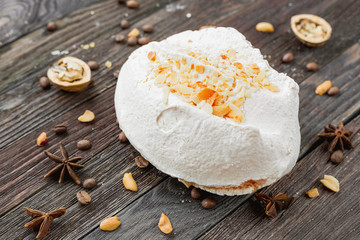 Big tasty meringue on rustic wooden background. Different spices around dessert - anise stars, coffee beans, walnuts and peanuts.