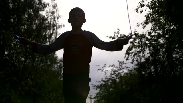 silhouette of boy jumping rope outdoors
