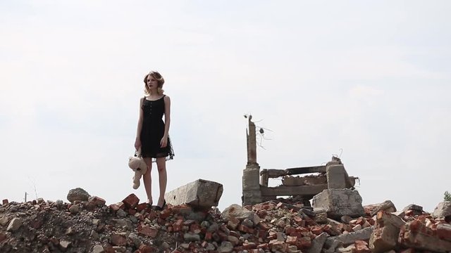 girl in a black dress with a toy bear goes on destruction of buildings