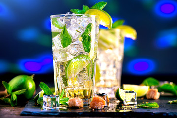 Mojito cocktail on a table. Summer cocktail with rum, lime, mint, ice cubes and brown sugar