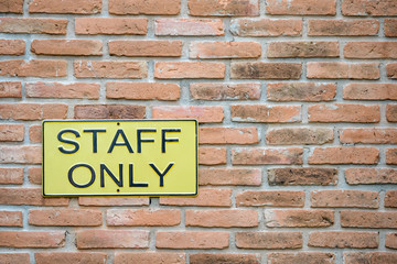 Yellow Staff only warning sign on retro style brick wall 