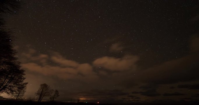Time-lapse pan of starlit sky behind clouds by a seashore with moonrise at the end