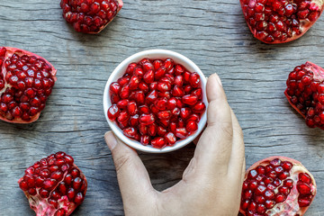 Fat Women Hand holding a white bowl of pomegranate seeds and pieces of pomegranate  on wooden background. Top view.