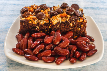 Red Kidney beans brownie, no flour prinkled with cashew nuts, dark chocolate chips and boiled red beans on blue wooden background. Clean Eating Homemade Healthy snack not fat. Selective focus.