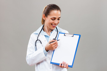 Beautiful female doctor is holding clipboard and showing document with pen. 