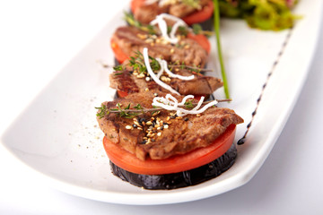 Beef medallions on tomato and grilled eggplant on a white plate