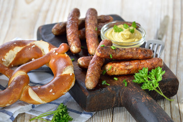 Acht gebratene Nürnberger Rostbratwürste mit Senf und Breze auf einem rustikalen Steakbrett...