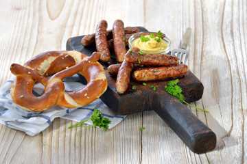 Acht gebratene Nürnberger Rostbratwürste mit Senf und Breze auf einem rustikalen Steakbrett...