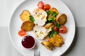 Stuffed chicken with baked potatoes with cherry tomatoes and cranberry sauce on a plate, top view