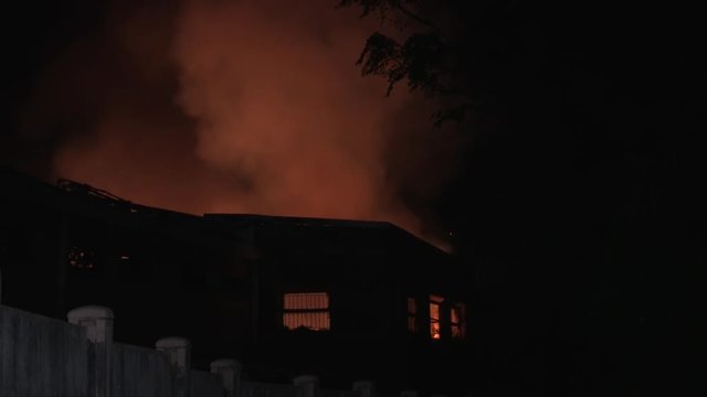 Flames and smoke blazing in night sky above burning building.