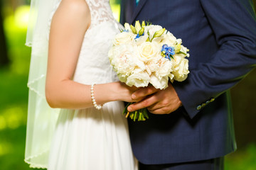 Wedding. The groom in a suit and the bride in a white dress standing side by side and are holding bouquets of white flowers. Summer, park