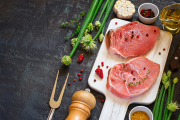 Raw fresh pork loin and spices on dark background. Top view with
