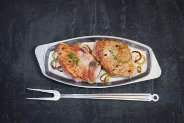 Roasted meat on a metal plate and fork on a dark background