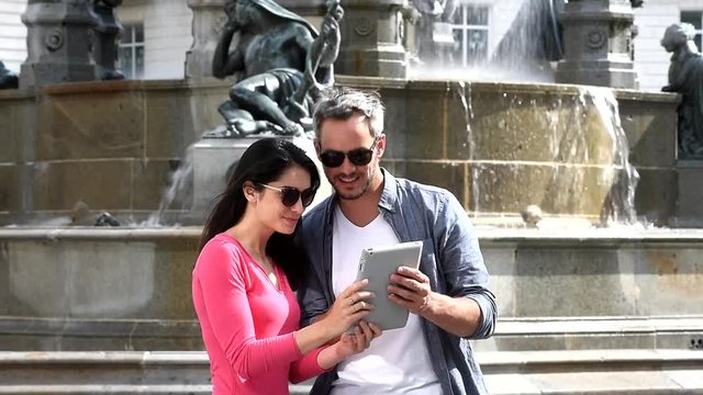 Summer in the city, a  couple of tourist near a fountain, is looking on tablet