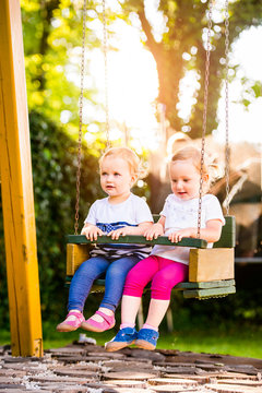 Two beautiful little girls swinging in the park.