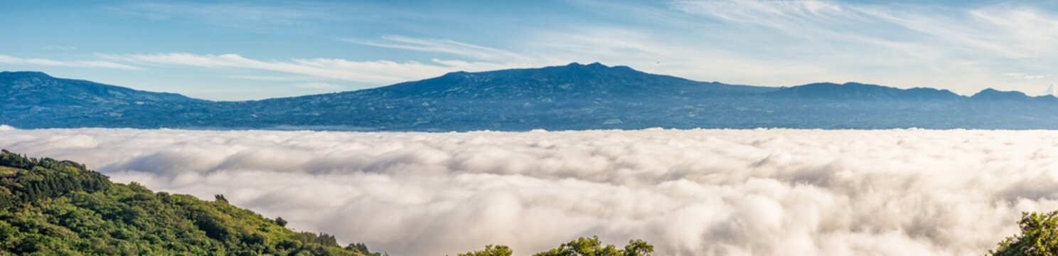 Fototapeta Barva volcano and near mountain ranges in the central valley of Costa Rica seen above the clouds that completly cover the city of San Jose the during the morning