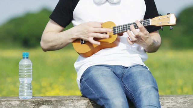 4K Close up of unseen person playing a ukulele in a rural environment, in slow motion