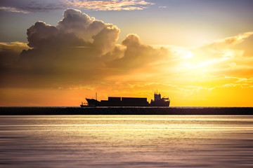 Naklejka premium Cargo ship in the ocean at sunset sky, Silhouette of the ship on a sunset, Industry Container cargo ship at coast in sunset sky, Transportation, Shipping, Logistics.