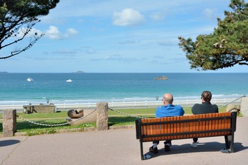 Couple assis sur un banc face à la mer à Perros-Guirec, plage de Trestraou. Bretagne