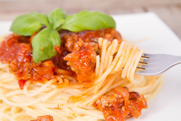 Spaghetti bolognese decorated with basil being eaten with a fork