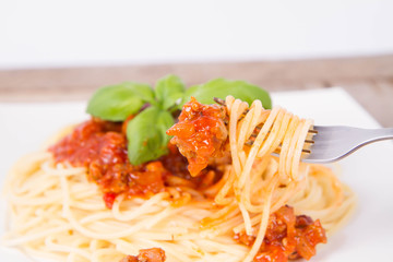 Spaghetti bolognese decorated with basil being eaten with a fork