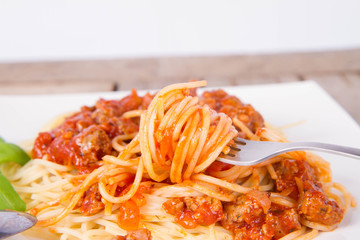 Spaghetti bolognese decorated with basil being eaten with a fork