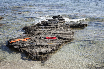dos trajes de neopreno rojo y naranja secándose al sol sobre una roca en la playa.