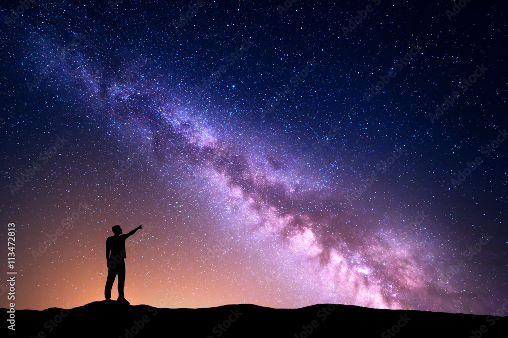 Wall mural milky way with silhouette of a standing man pointing finger in night starry sky on the hill. colorfu
