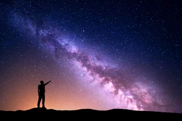 Foto auf Acrylglas Milchstraße mit Silhouette eines stehenden Mannes, der mit dem Finger in den nächtlichen Sternenhimmel auf dem Hügel zeigt. Bunte Nachtlandschaft. Schönes Universum, Reisehintergrund mit gelbem Licht des purpurroten Himmels. Platz © den-belitsky