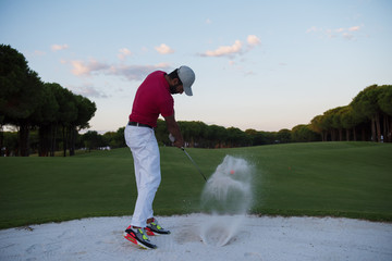 golfer hitting a sand bunker shot on sunset