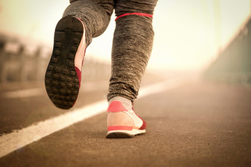 Runner athlete feet running on road under sunlight