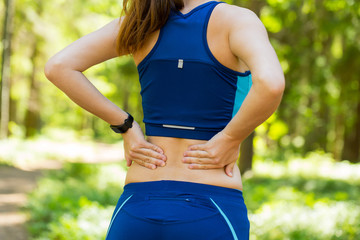 Back pain. Young woman in blue sportswear with smartwatches rubb