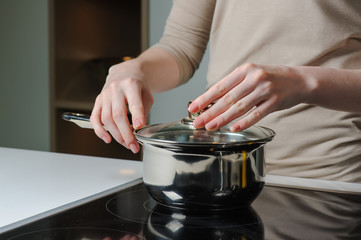 Female hand holding the lid of the pan. Person removing lid from cooking pot.