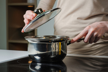 Female hand holding the lid of the pan. Person removing lid from cooking pot.