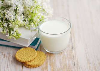 Milk mug, cookies and books with a bouquet of a white lilac on a wooden surface. 