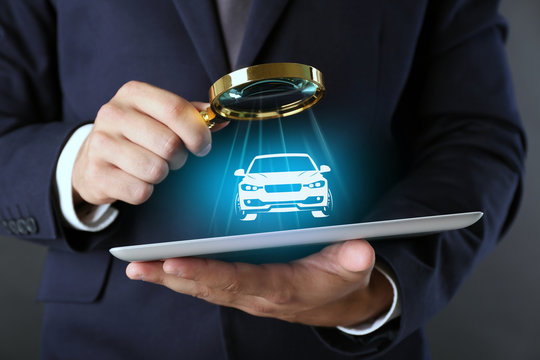 Businessman Holding Magnifying Glass And Digital Tablet With Virtual Car On Dark Grey Background