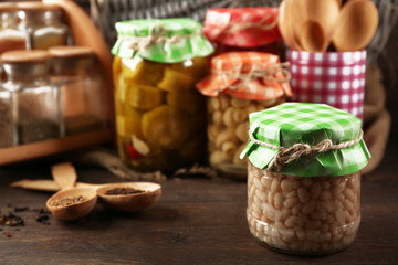 Jars with pickled vegetables, beans, spices and kitchenware on wooden background