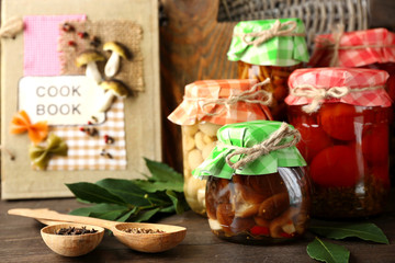 Jars with pickled vegetables, beans, spices and kitchenware on wooden background