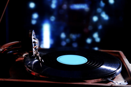 Turntable with vinyl record on dark blurred background