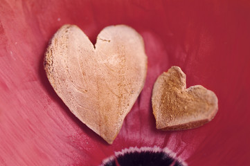 Obraz na płótnie Canvas Two decorative hearts on poppy red petals close up. Romantic background by St. Valentine's Day, a wedding.