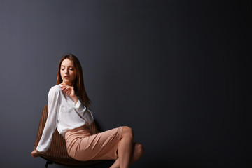 Beautiful young woman sitting in a chair on grey wall background