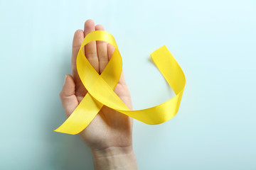 Hand holding yellow ribbon on light grey background