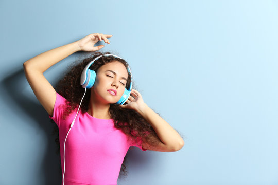 African American woman listening to music in headphones on grey background