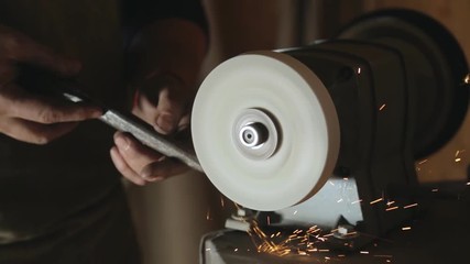 A blacksmith sharpening a workpiece on a grinding lap closeup.