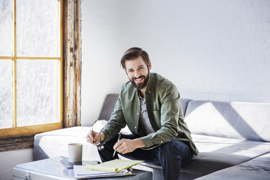 Portrait of smiling businessman writing in book while sitting in creative office