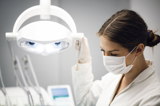 Female dentist adjusting illuminated lamp in clinic