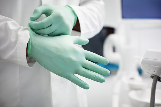 Mid section of doctor wearing surgical gloves in clinic 