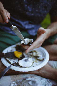 Low section of man shucking oyster shell while sitting on blanket at lawn